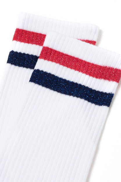 A pair of white ribbed socks featuring two horizontal stripes in shimmering red and dark blue at the cuffs.