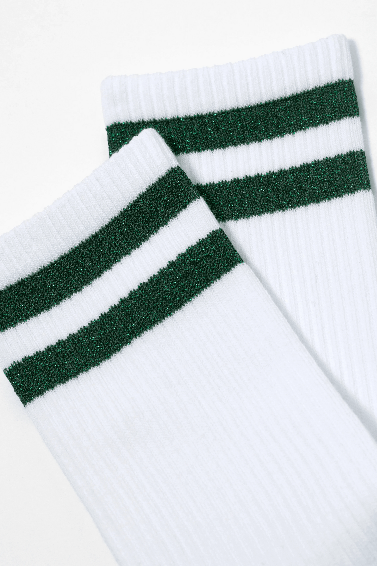 A pair of white crew socks features two horizontal, shimmering green glitter stripes near the top ribbed cuff.