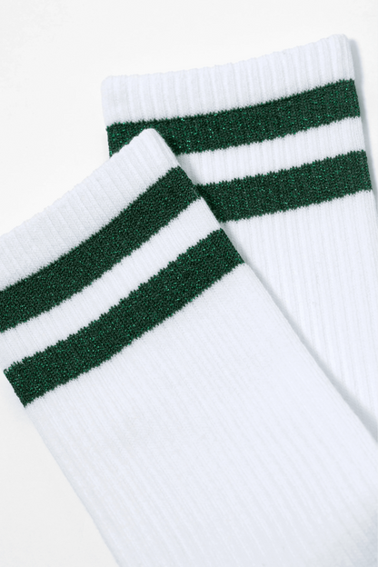 A pair of white crew socks features two horizontal, shimmering green glitter stripes near the top ribbed cuff.
