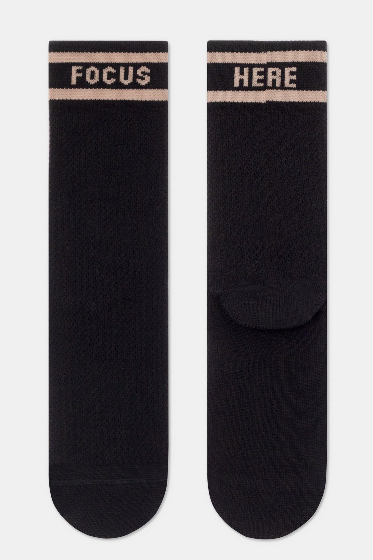 A pair of black crew-length socks featuring two horizontal light beige stripes near the top, with the word FOCUS printed on the left sock and the word HERE on the right sock in a matching light beige font.