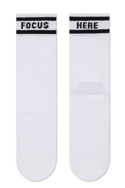 A pair of white mid-calf socks with black stripes at the top, featuring the word FOCUS printed on the left sock and the word HERE printed on the right sock.