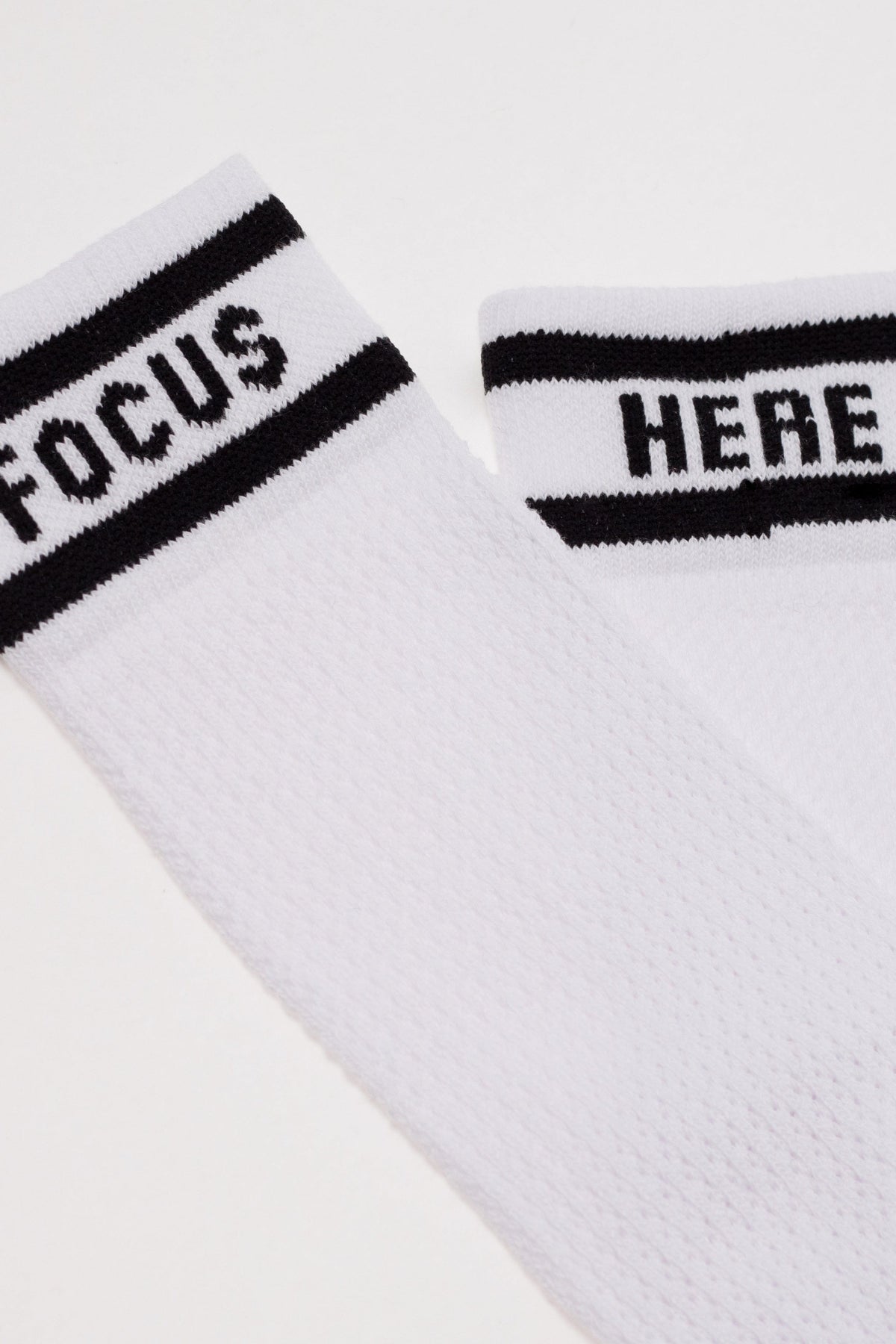 A pair of white crew socks with black horizontal stripes and the words FOCUS and HERE knitted into the cuffs.