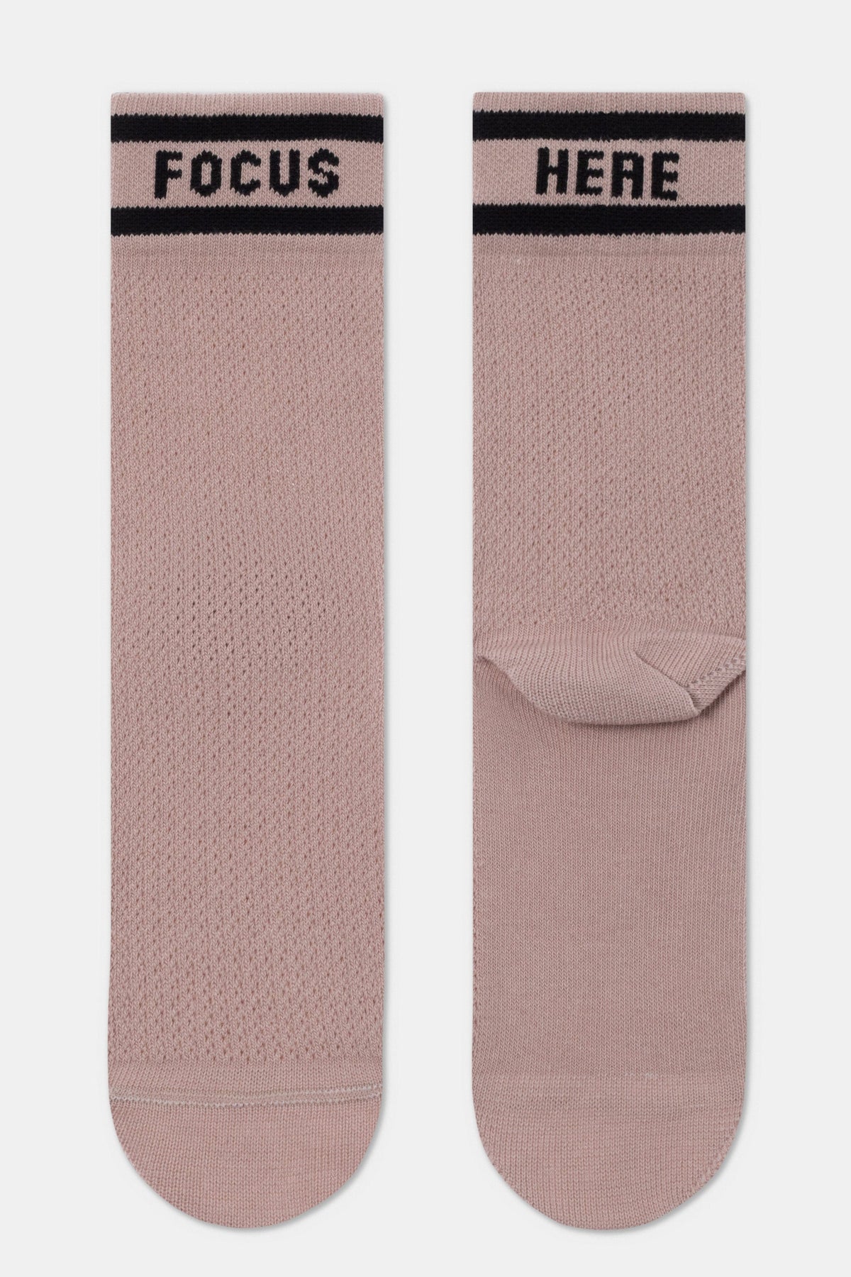 A pair of dusty pink crew socks featuring the word FOCUS on the left sock and HERE on the right, both accented by two black horizontal stripes at the cuff.