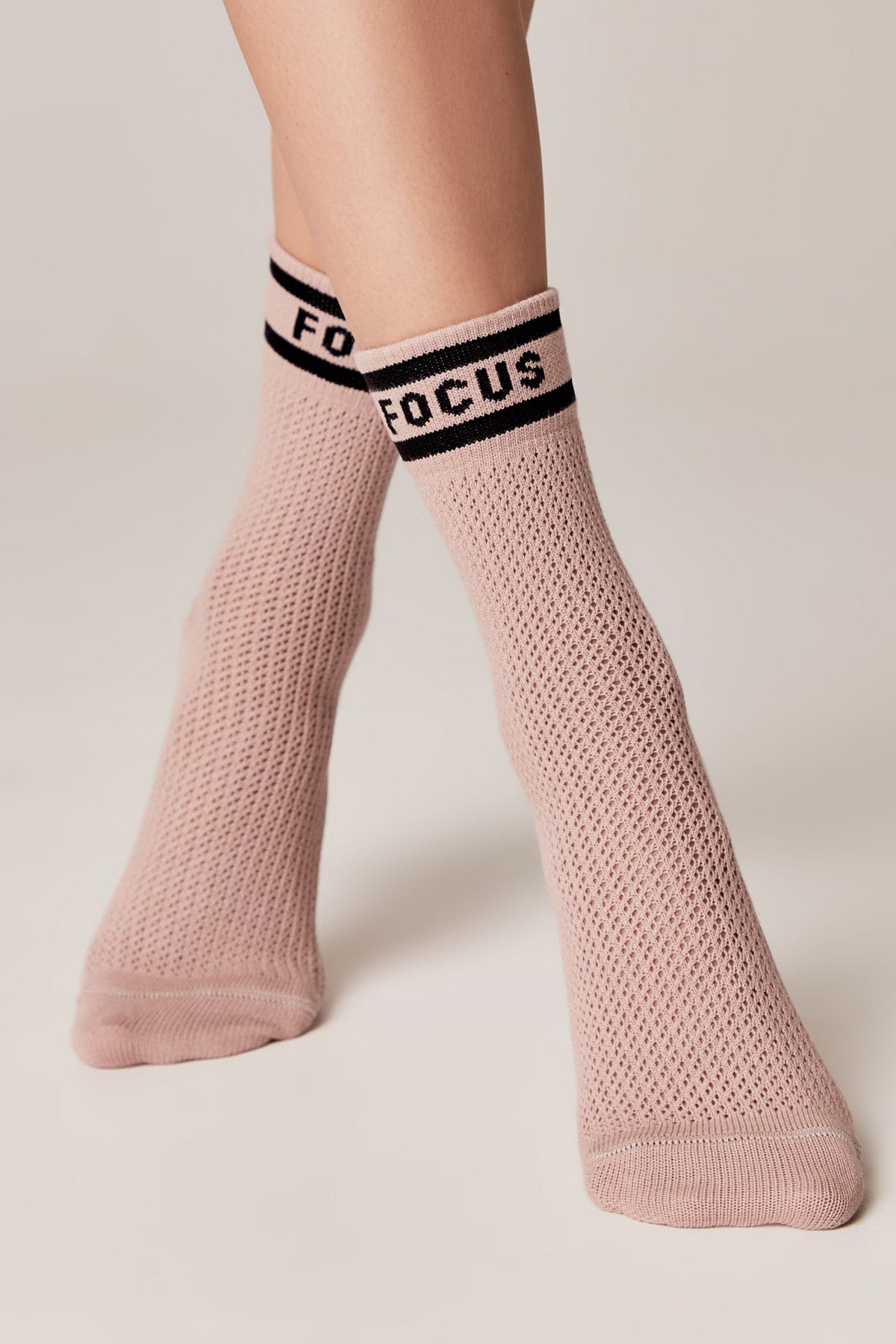 Light pink crew-length socks with a textured mesh knit pattern and a black ribbed cuff featuring the word FOCUS in bold white letters, worn on feet against a plain light background.