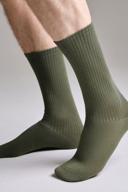 Olive green ribbed crew socks worn on a pair of legs against a plain light gray background.