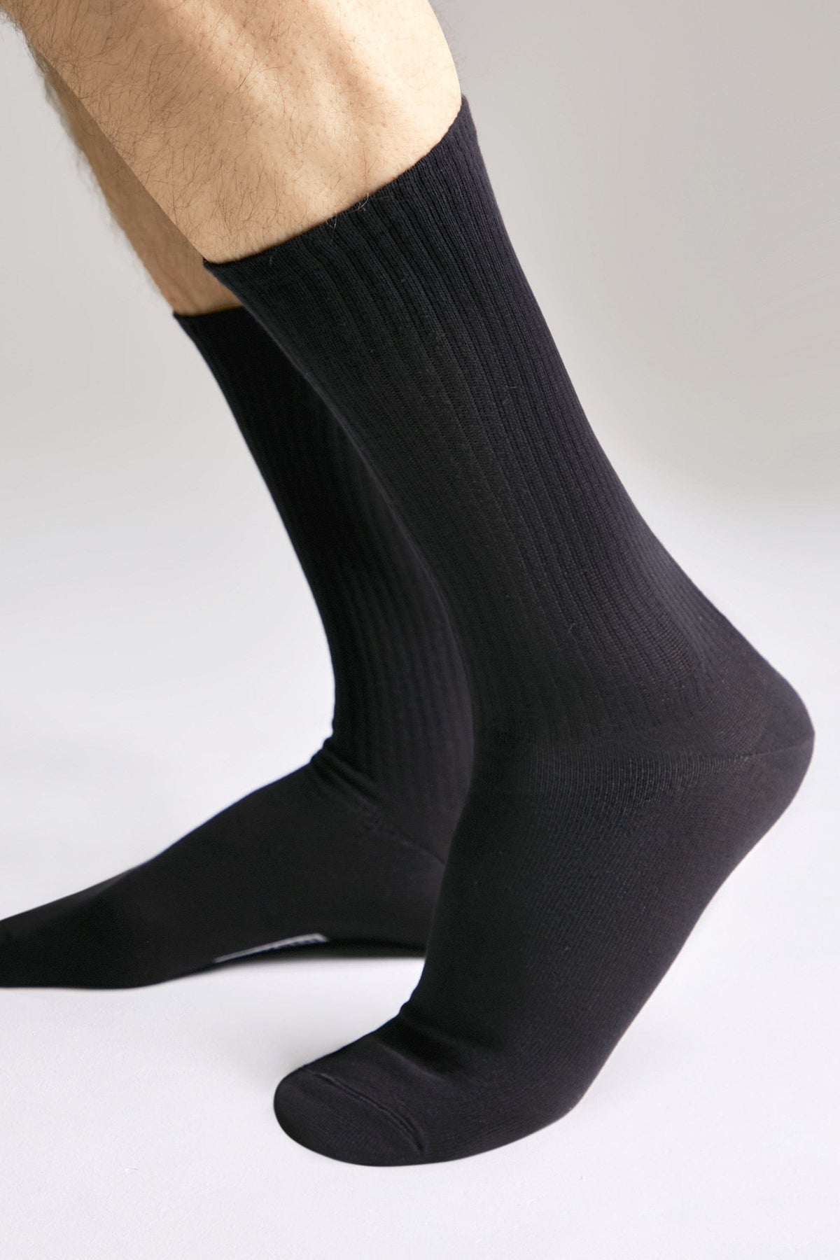 A pair of black ribbed crew socks worn on a person's feet against a plain white background.