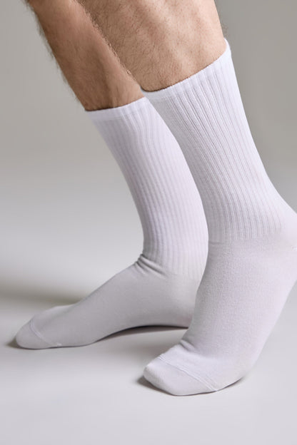 A pair of plain white crew socks worn on a person's feet against a neutral light grey background.