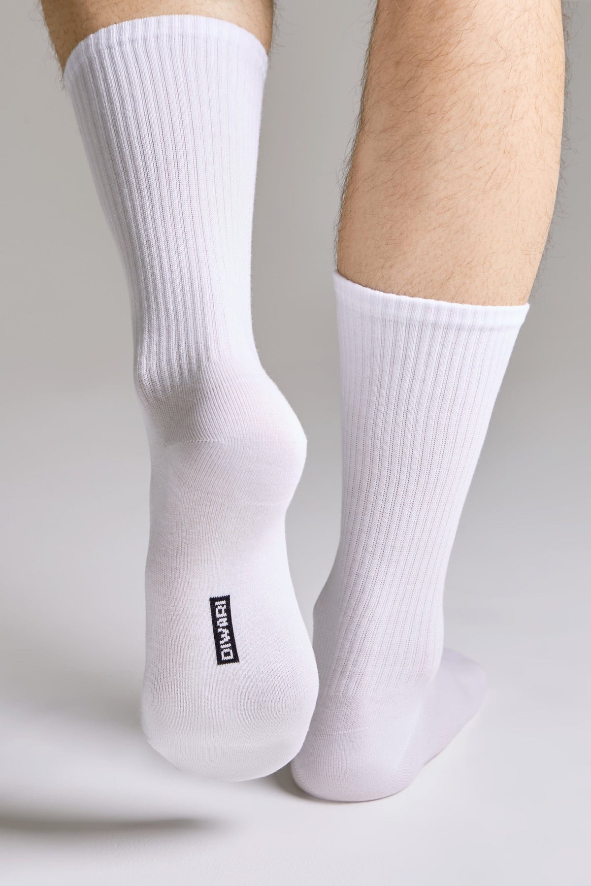 A pair of white ribbed mid-calf socks worn on a person's feet against a light grey background, featuring the brand name printed in black on the sole of one sock.