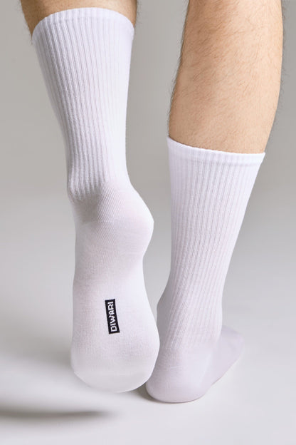 A pair of white ribbed mid-calf socks worn on a person's feet against a light grey background, featuring the brand name printed in black on the sole of one sock.