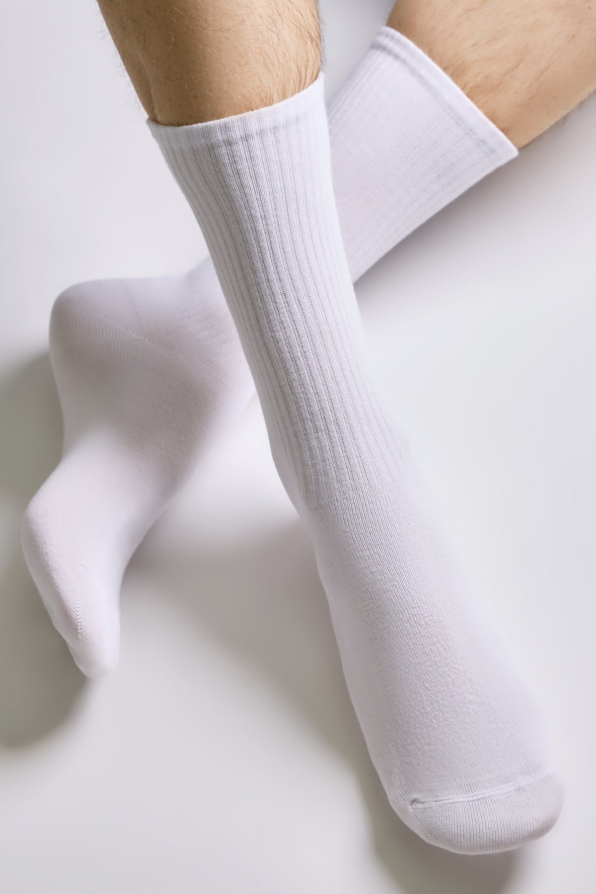 A pair of plain white ribbed crew socks worn on a person's legs against a plain white background.