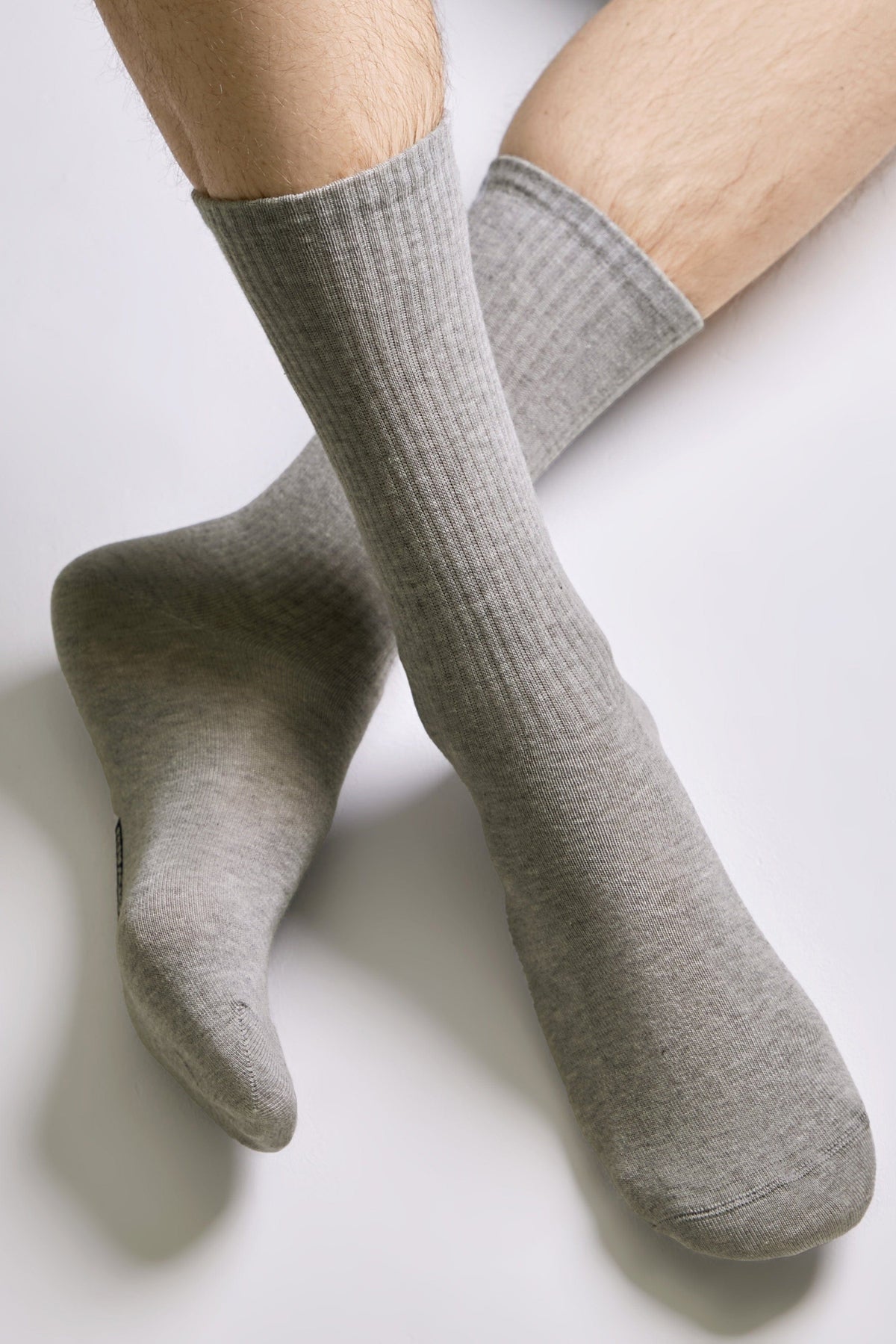 A pair of light grey ribbed crew-length socks worn on a person's feet against a plain white background.