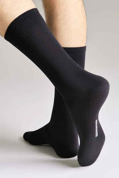 A pair of black ribbed crew socks worn on a person's feet against a plain light gray background.