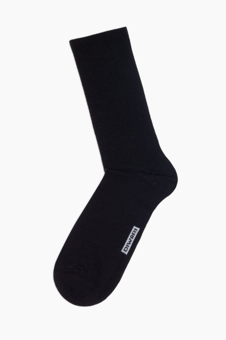 A solid black crew-length sock with a small white rectangular brand logo label on the side.