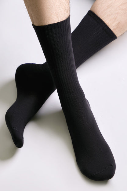 A pair of black crew socks worn on a person's feet against a plain white background.