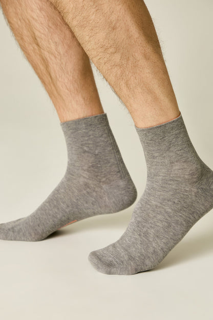 A pair of mid-calf heather grey socks on a person's feet, set against a plain light background.