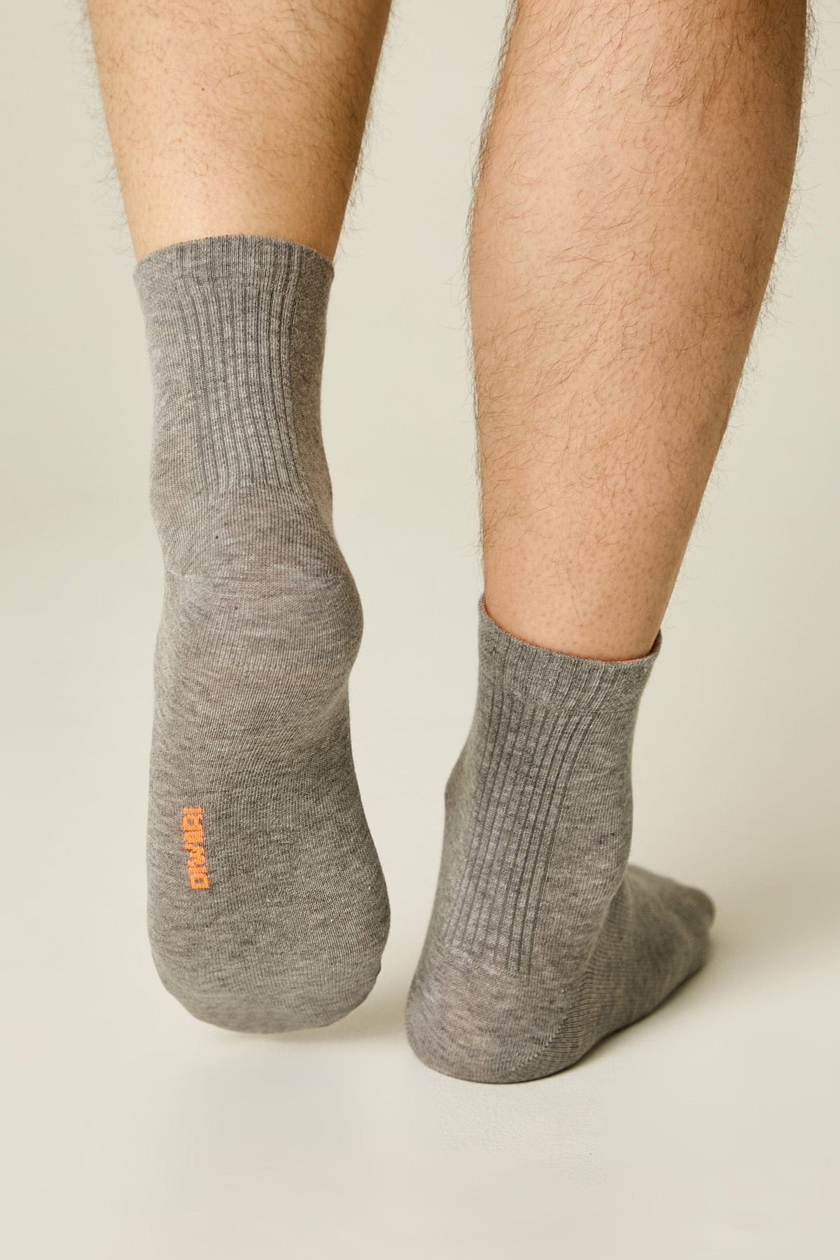 A pair of grey ribbed mid-calf socks worn on legs, with the brand name printed in orange on the bottom of the left foot.