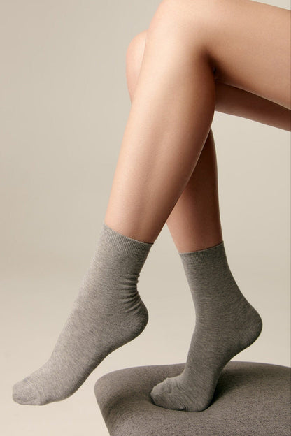 A pair of mid-calf grey socks worn on a person's feet, with one foot resting on a dark grey stool against a plain light background.