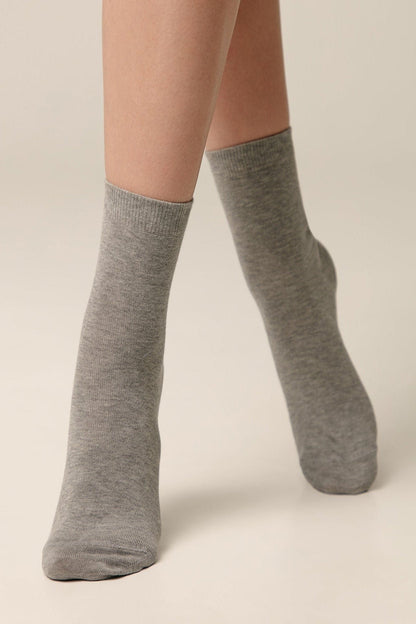 A pair of crew-length light grey socks worn on a pair of legs against a plain light background.