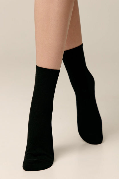 A pair of simple black socks worn on a model's feet against a plain light background.