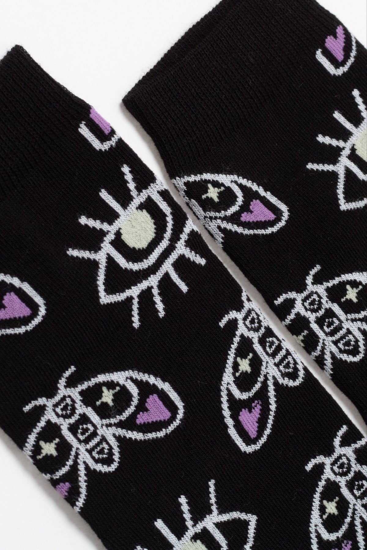 A pair of black socks featuring a repeating pattern of white outlined moths and eyes with light green and purple accents.