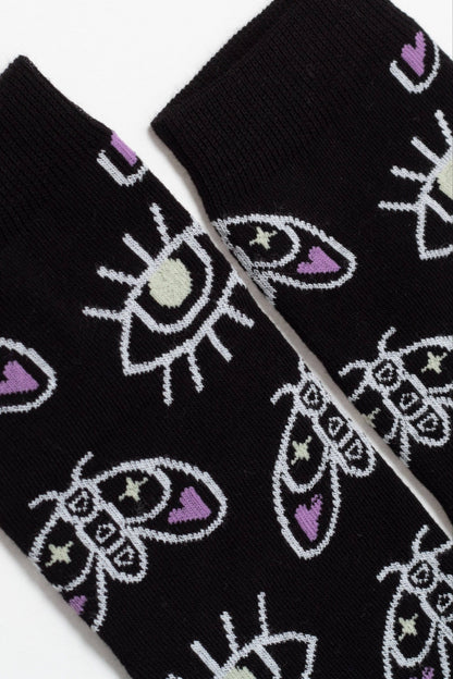 A pair of black socks featuring a repeating pattern of white outlined moths and eyes with light green and purple accents.