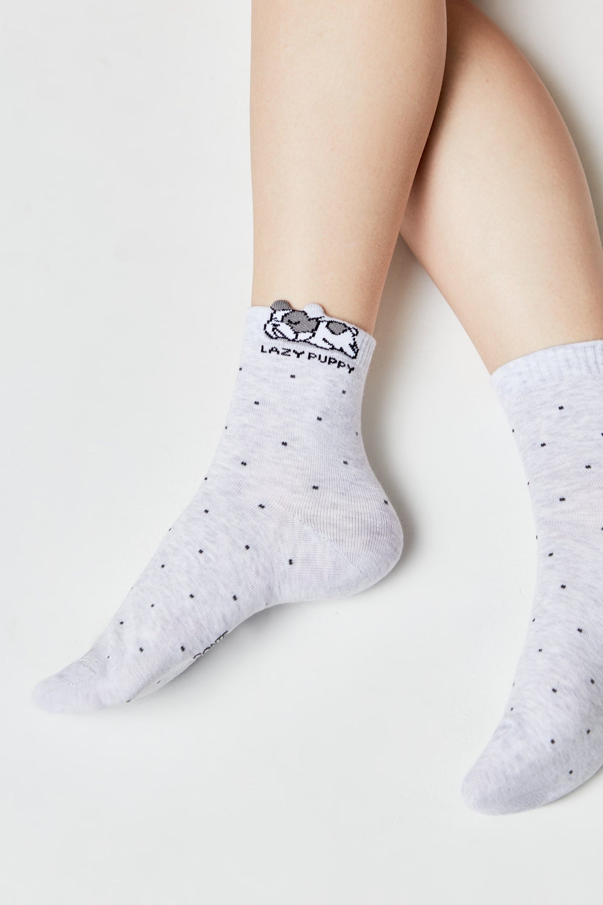 A pair of light grey ankle socks featuring a subtle pattern of tiny dark dots and a graphic of a resting puppy with the words LAZY PUPPY embroidered at the top.