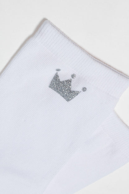 A white ribbed ankle sock features a small, sparkly silver crown icon embroidered on the side.