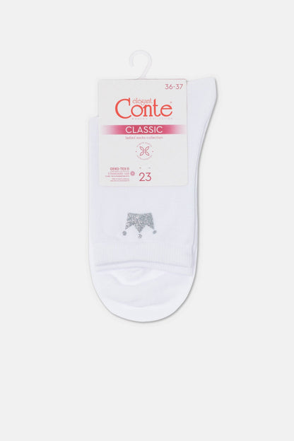 A pair of white ankle socks features a small silver glittery crown design on the front and is attached to a branded paper packaging header.