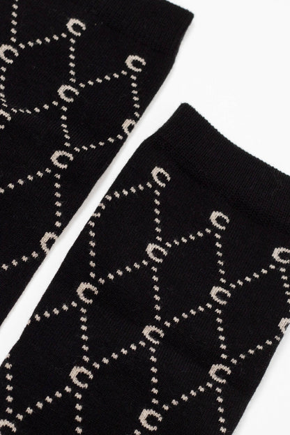 Two black socks laid side by side on a white surface feature a repeating beige geometric pattern of interlinked circles and lines.