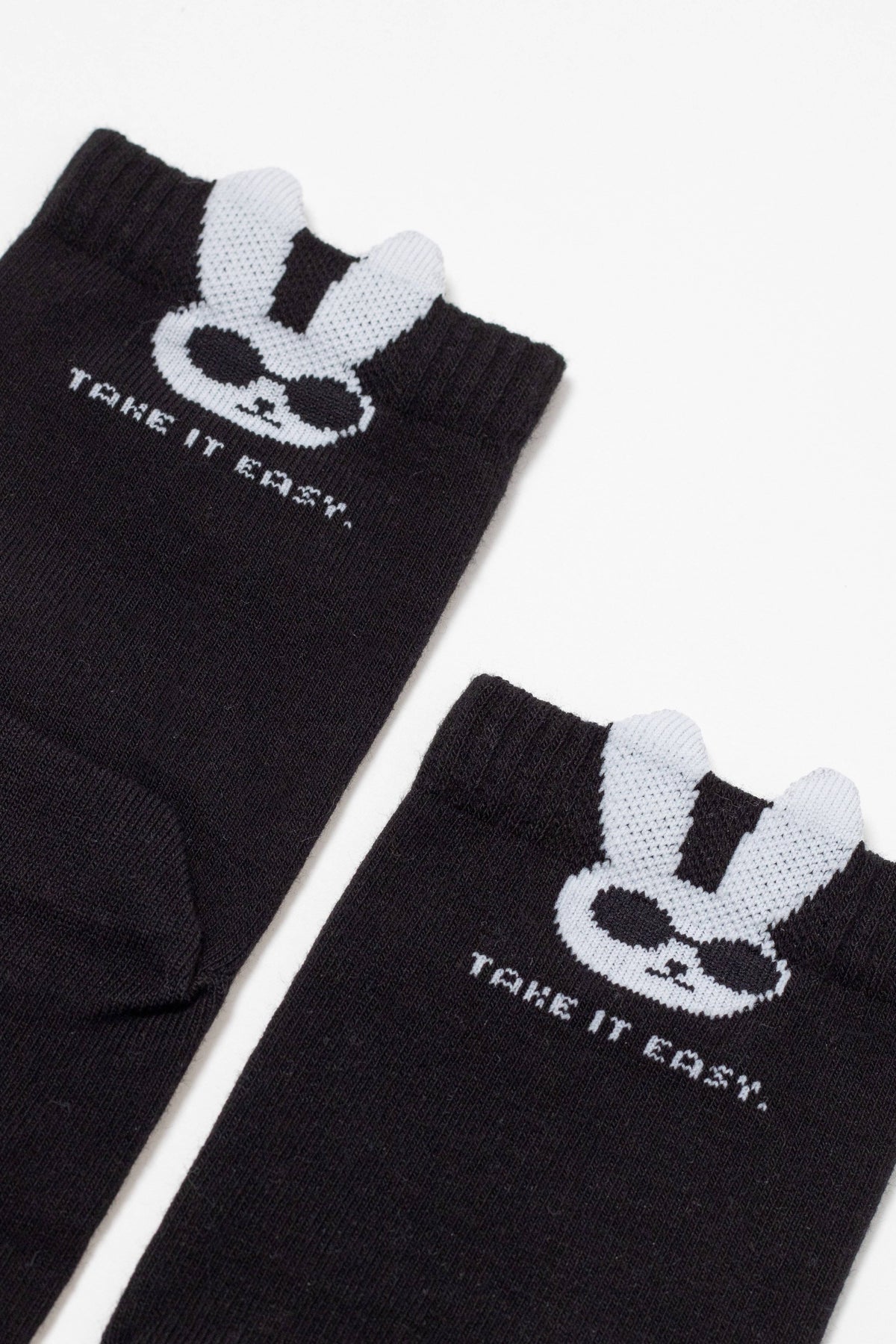 A pair of black socks featuring a graphic of a white bunny wearing sunglasses and the text "TAKE IT EASY." printed below, with two small white bunny ears extending from the ribbed cuffs.