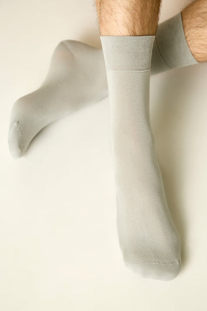 A pair of light grey, calf-length socks worn on a person's legs against a plain white background.