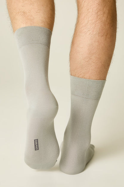 A person wearing a pair of light grey mid-calf socks with a small black rectangular logo on the heel of the left sock.