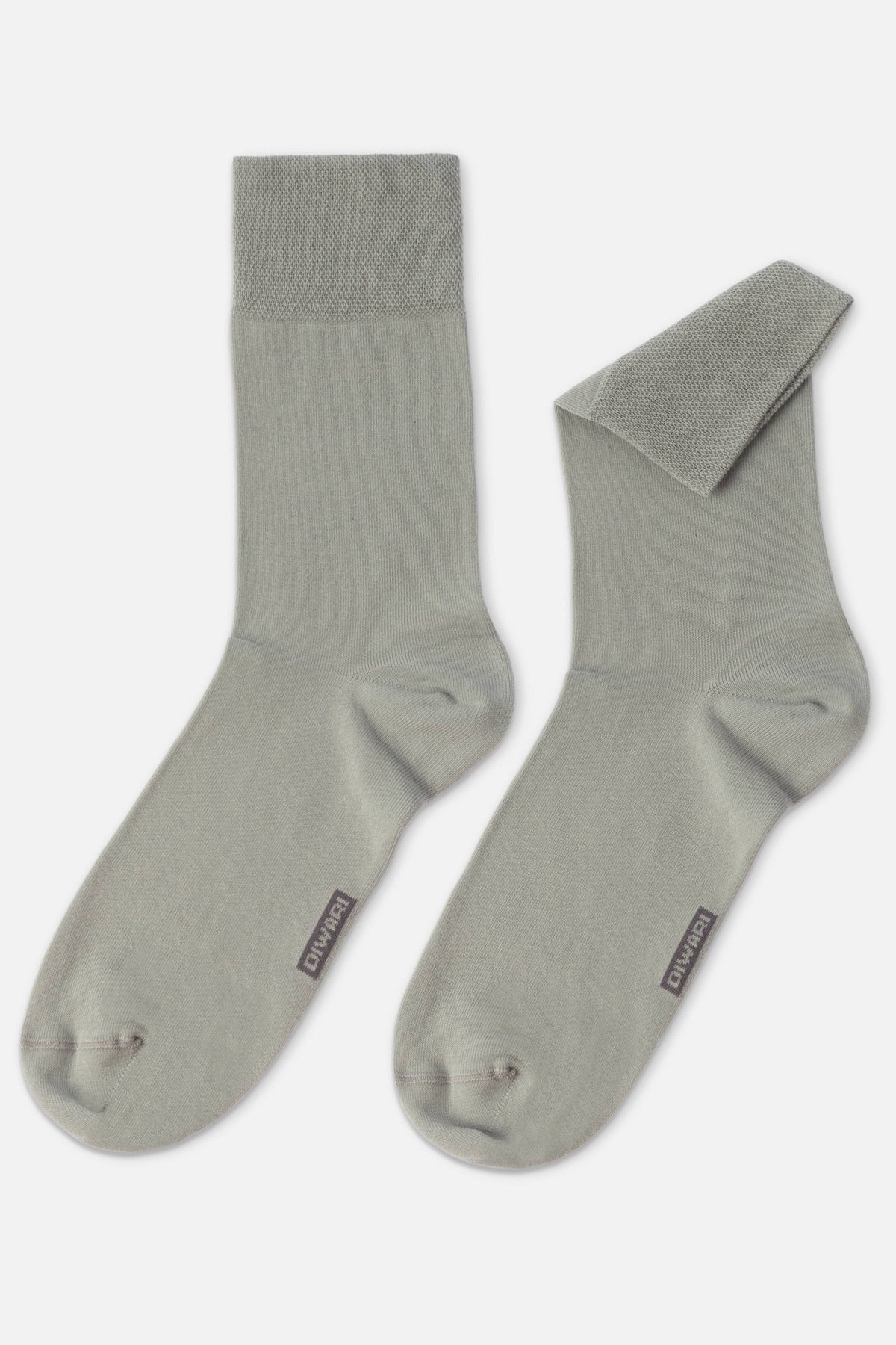 A pair of sage green crew socks with a textured cuff and a small logo tag on the side of each foot.