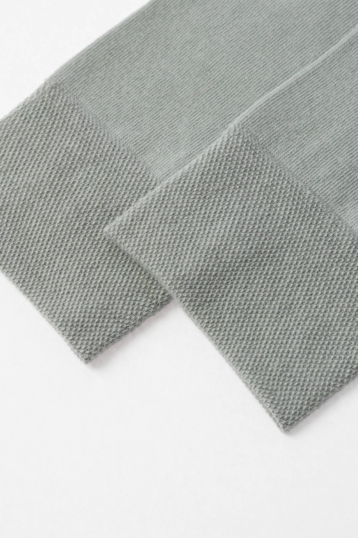 A pair of folded sage green socks with ribbed cuffs shown against a plain white background.
