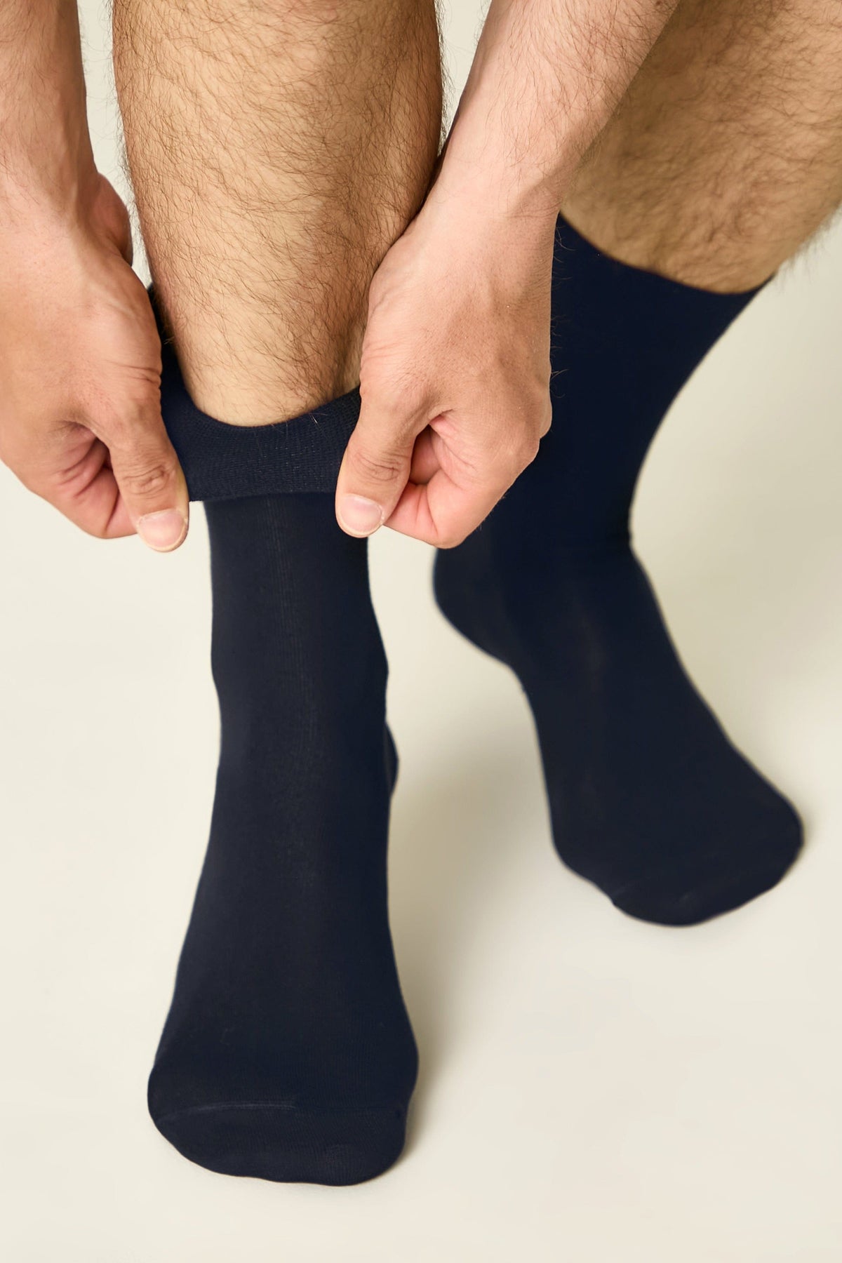 A pair of plain navy blue crew socks being pulled up onto a person's lower leg.