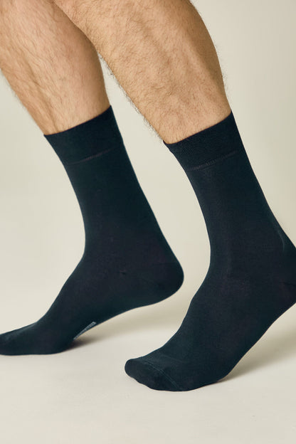 A pair of solid black crew-length socks worn on a person's lower legs against a neutral background.