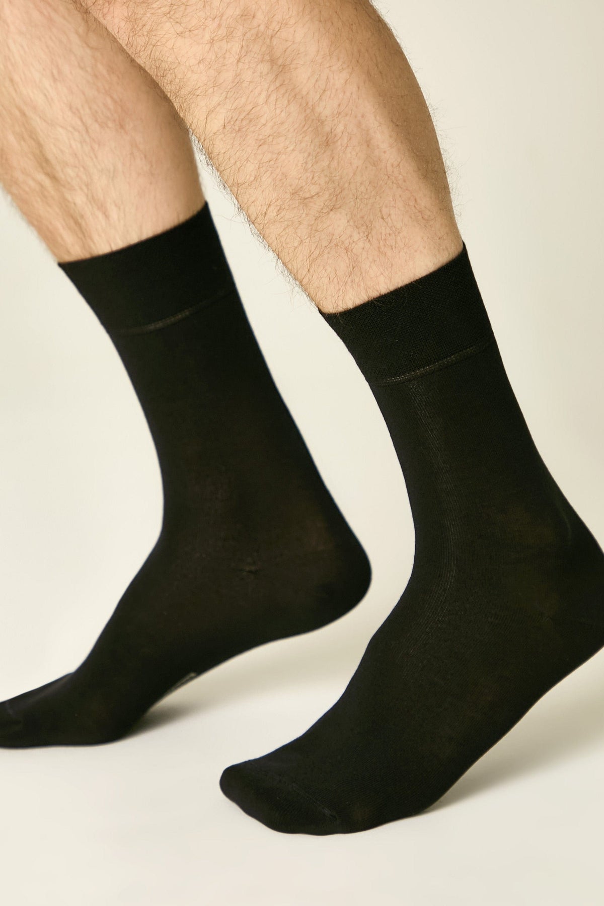 A pair of black crew-length socks worn on a pair of legs against a plain light background.