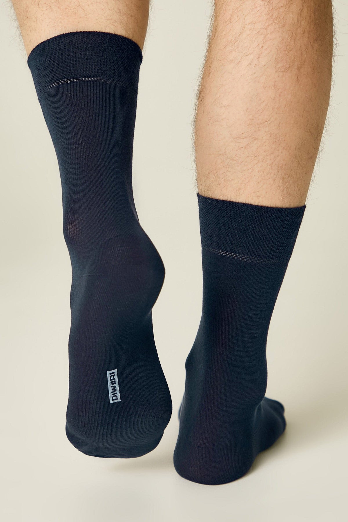 A pair of dark navy blue mid-calf socks worn on a person's feet, featuring a small white rectangular logo printed on the heel of the left sock.