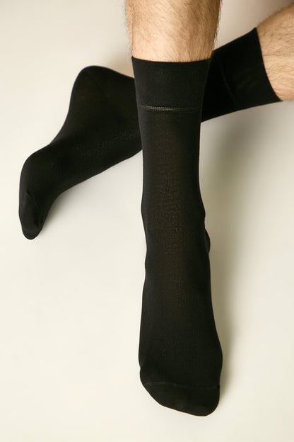 A pair of black crew-length socks worn on a person's legs against a plain, light background.