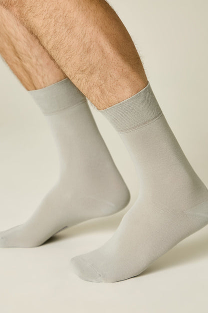 A pair of light grey mid-calf crew socks worn by a person with hairy legs against a plain light-colored background.