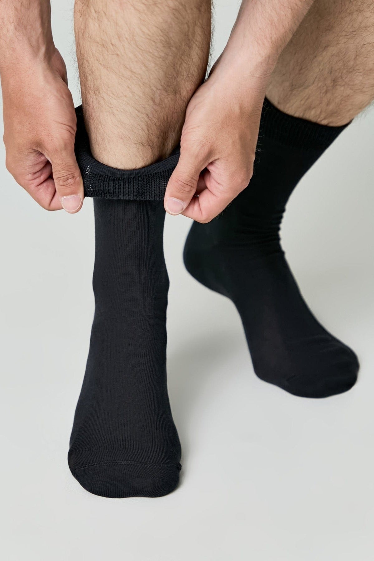 A pair of black crew socks being pulled up onto the calves by a pair of hands.