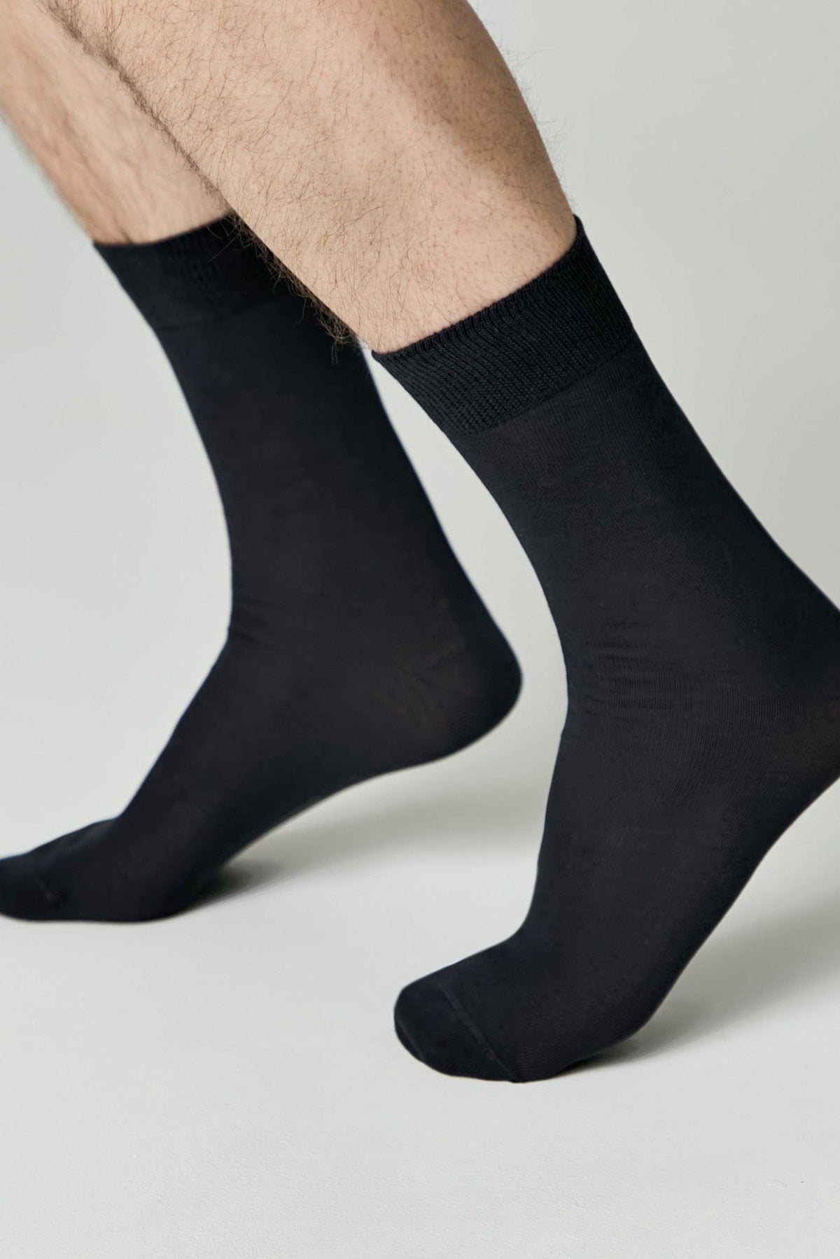 A pair of black crew socks worn on a person's feet against a plain light gray background.