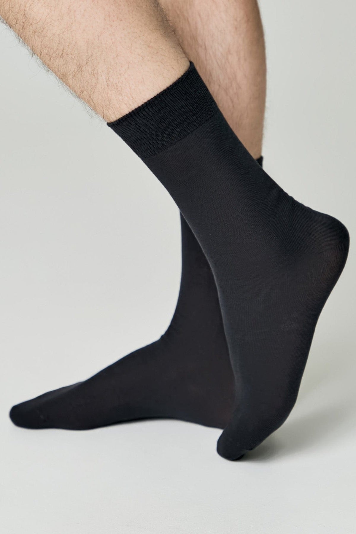A pair of black crew socks worn on a person's feet against a plain light gray background.
