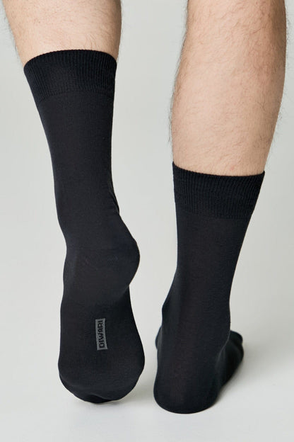 A pair of plain black calf-length socks worn on the lower legs of a person against a light gray background.