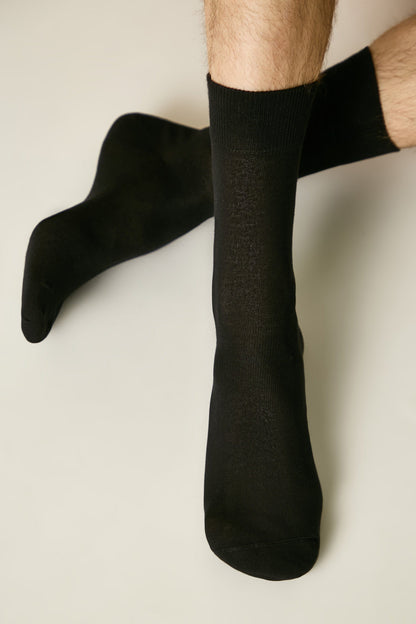 A pair of black crew-length socks worn on a person's feet against a neutral background.