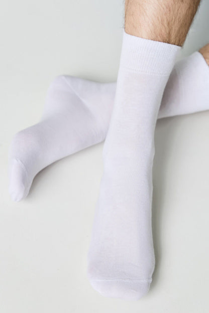 A pair of plain white crew socks worn on a person's feet against a neutral background.