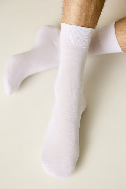 A pair of plain white crew socks worn on a person's feet against a light cream background.