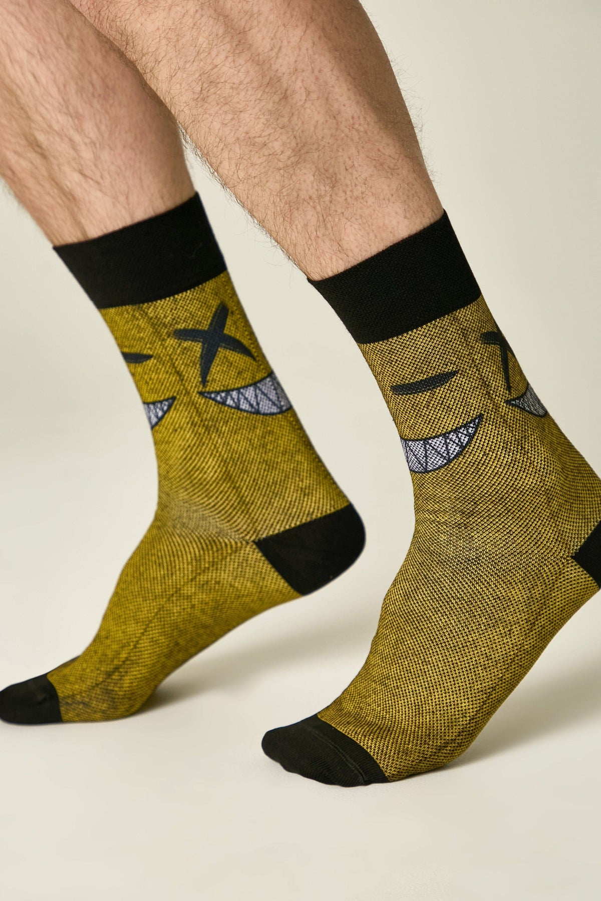 Crew socks in a mustard yellow textured knit feature a black graphic of a mischievous smiling face with X-shaped eyes and black cuffs and toe caps.