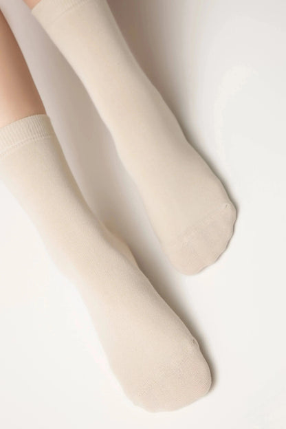A pair of plain beige crew socks worn on a person's feet against a plain white background.