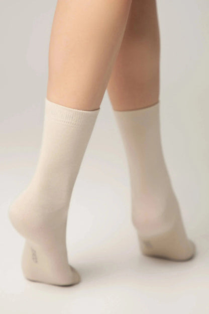 A pair of beige crew socks worn on a person standing on their tiptoes against a neutral background.